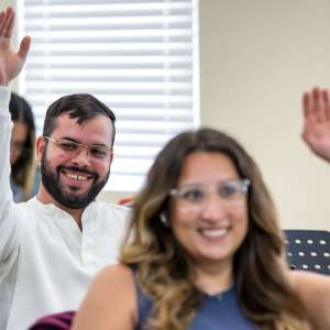 Student in Glasses Raising Hand to Contribute his Thoughts in MUA Classroom.