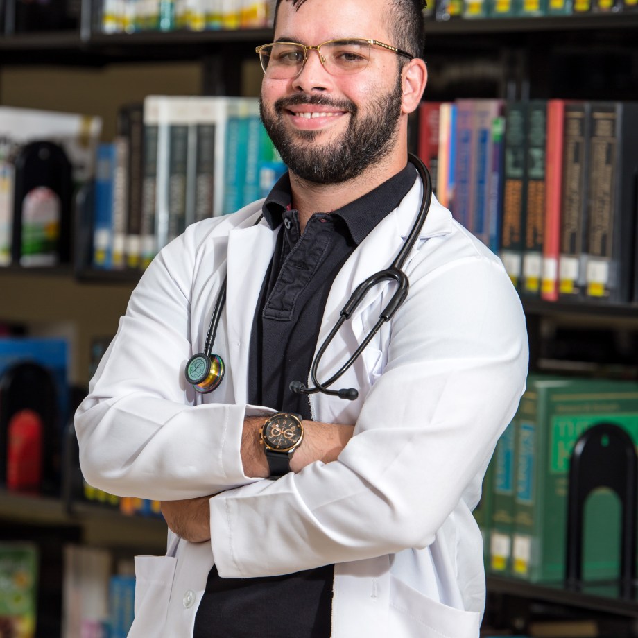 MUA Student Standing in Front of a Library, Wearing a White Coat and Stethoscope
